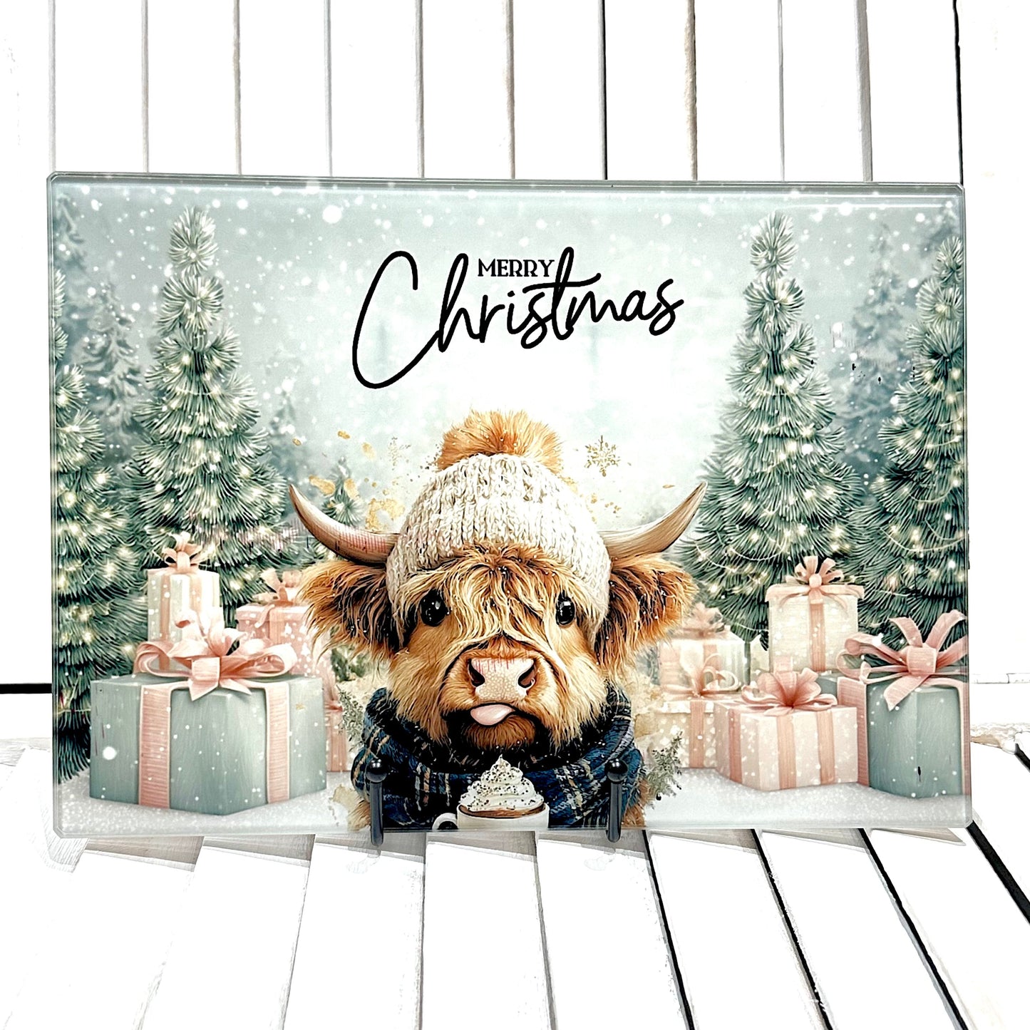 Christmas card with a Highland cow wearing a hat and scarf, surrounded by presents and trees.