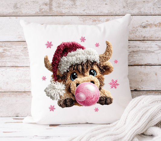 Decorative pillow with a highland cow wearing a Santa hat and blowing a bubblegum bubble on a wooden background.